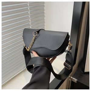 Detail of a black leather saddle bag featuring a gold chain and wide woven strap