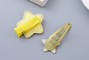 Detailed view of yellow fabric-wrapped and gold glitter star hair clips with snap closure