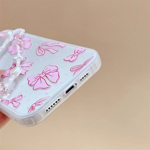 Close-up of clear phone case featuring pink bow pattern and beaded phone strap