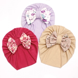 Close-up of soft cotton baby hats with large floral bow knots in pink, purple and beige
