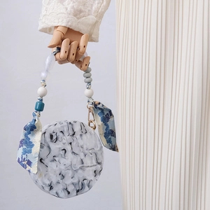Macro detail of round marble acrylic handbag featuring beaded handle and silk scarf
