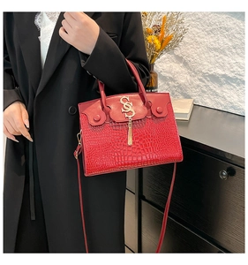 Close-up of red crocodile pattern leather handbag with gold S-shaped logo and tassel