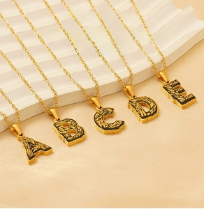 Close-up of gold stainless steel initial pendants with vintage black textured inlay