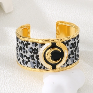 Detail of gold moon face on black enamel with leopard pattern on a wide metal cuff bracelet