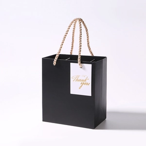 Detail view of black gift bag featuring golden Thank You tag and woven rope handles