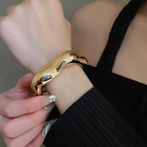 Close-up of a gold wavy cuff bracelet with a polished mirror finish on the wrist