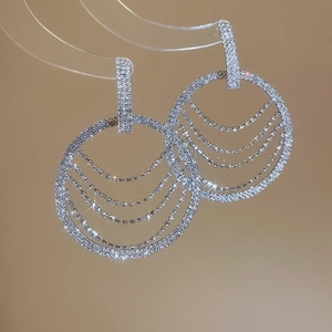 Détail de boucles d'oreilles créoles argentées avec franges en cristal et strass brillants
