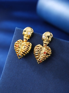 Macro detail of gold skull heart earrings with red cubic zirconia on blue velvet