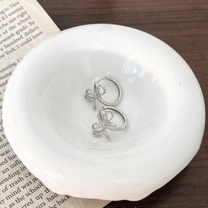 Polished silver hollow bow earrings in a minimalist hoop style on a white ceramic dish