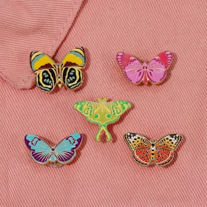 Set of five colorful enamel butterfly and moth brooches on pink denim background
