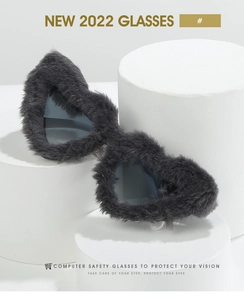 Detail of plush black faux fur frame heart sunglasses with dark grey lenses on white pedestals