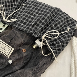Detail of plaid and denim patchwork backpack featuring drawstrings and heart buttons