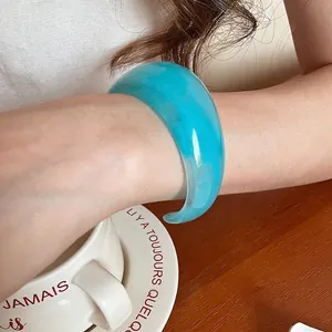 Minimalist wide resin cuff bracelet with blue marble texture on a wooden table
