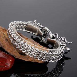 Vue détaillée du bracelet tête de dragon argenté avec chaîne double sur pierre et bois