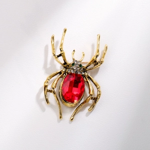 Elegant gold spider brooch with large red gemstone and sparkling green crystal eyes
