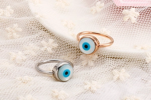 Close-up of rose gold and silver rings set featuring blue evil eye motif on lace background