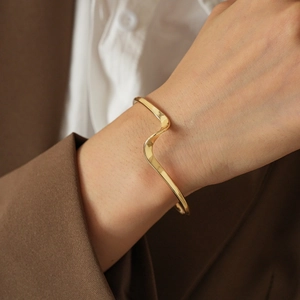 Macro shot of minimalist gold wavy bangle bracelet with a high-polished metallic finish
