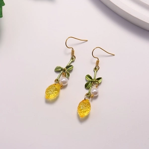 Detailed view of yellow lemon earrings with green leaves and white pearls on golden hooks