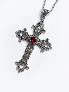 Macro shot of silver gothic cross pendant with red gemstone and floral relief pattern