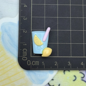 Macro shot of 2cm blue resin lemonade charm with ruler on a black grid cutting mat