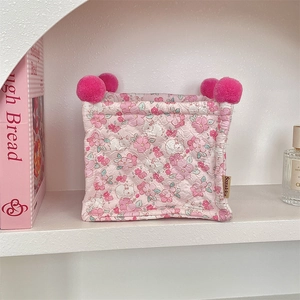 Quilted floral storage basket with pink pom-poms on a white shelf for desk organization