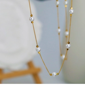 Close-up of golden titanium necklace featuring five pearls and geometric accents