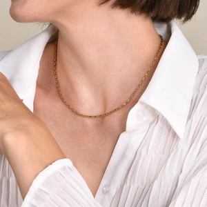 Detail of a minimalist gold box chain necklace worn by a model for a layered jewelry look