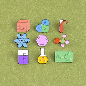 Flat lay of nine colorful chemistry enamel pins with molecular structures on green background