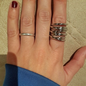 Close-up of stylish multi-layer silver spring rings worn on a hand against a beige background