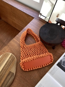 Close-up of orange cotton rope woven tote bag with a flat base on a wooden desk