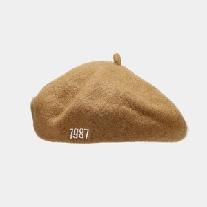 Close-up of the white 1987 embroidery and high-density wool texture on a camel beret