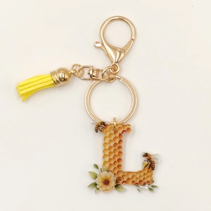 Detail of letter L acrylic keychain with honeybee hive pattern and yellow tassel