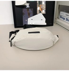 Detail of a creamy white nylon chest bag featuring a black adjustable strap and buckle
