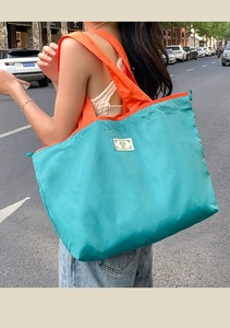 Detail of teal and orange foldable oxford tote bag with BEST label on urban street