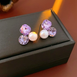 Detail of luxury triangle earrings with purple crystals and white pearls on a black box