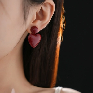 Close-up of deep red heart-shaped earrings with a glossy finish on a model's ear