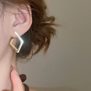 Close-up of golden geometric rhombus earrings worn by a model in a minimalist style