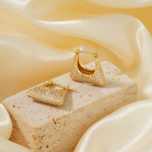 Macro detail of gold hoop earrings with pavé zircon inlay on textured stone background