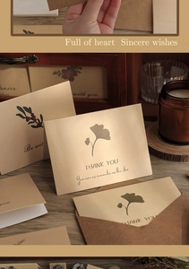 Close-up of vintage ginkgo leaf thank you card with kraft envelope on a wooden desk