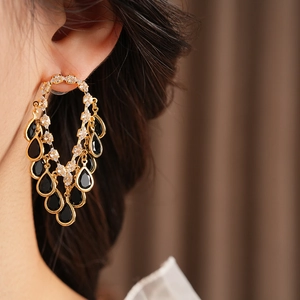 Close-up of gold hoop earrings with black teardrop crystals and sparkling zircons on model