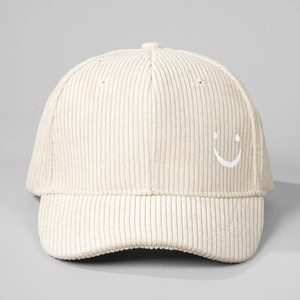 Close-up detail of beige corduroy baseball cap with white embroidered smiley face on side