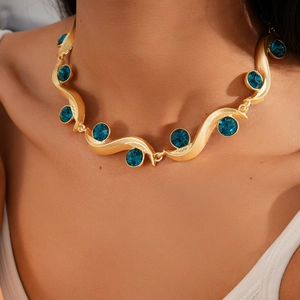 Close-up of gold wavy necklace featuring vibrant teal crystals on model neckline