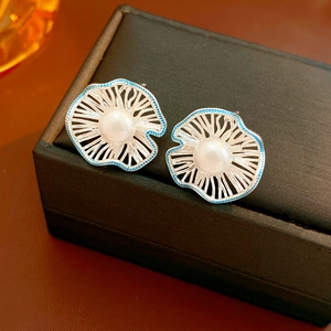 Detailed close-up of hollow flower earrings with white pearl and blue enamel accents