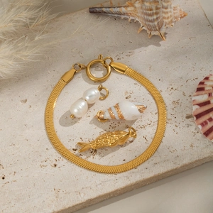 Dettaglio di un bracciale a catena serpente dorata con ciondoli perla, conchiglia e pesce