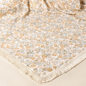 Macro detail of breathable cotton gauze baby blanket with floral pattern and tassels