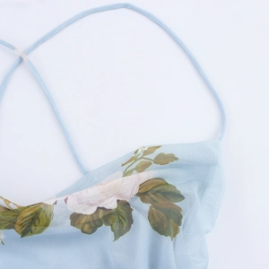 Détail d'une robe fleurie bleu clair avec de fines bretelles et décolleté à volants