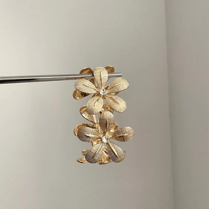 Elegant gold flower earrings with layered petals and crystal center on metal stand