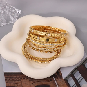 Detail view of stackable gold-plated crystal bangles on a white ceramic tray