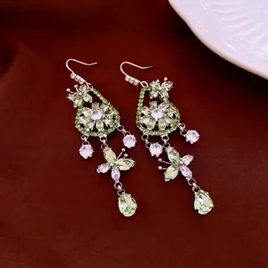 Elegant silver drop earrings with green zircon butterfly floral design on red background