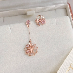 Detailed close-up of asymmetrical flower earrings with pink zircons in rose gold setting